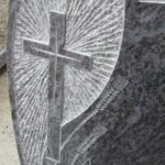 Detajl nagrobnika z vklesanim križem in kamnitim reliefom v granitu.