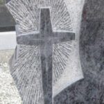Granitni detajl nagrobnika z izrazitim reliefom in izklesanim križem.