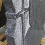 Detajl nagrobnika z vklesanim križem in kamnitim reliefom v granitu.