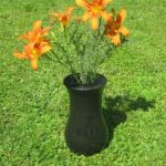 Klasična granitna nagrobna vaza z oranžnimi cvetovi na travi.