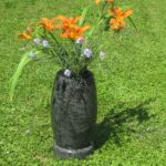 Visoka granitna nagrobna vaza z oranžnimi lilijami na zeleni podlagi.