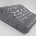 Kamnit nagrobni blok v obliki knjige z več vpisanimi imeni in datumi.